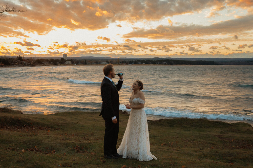 groom drinks champagne at sunset in marquette elopement